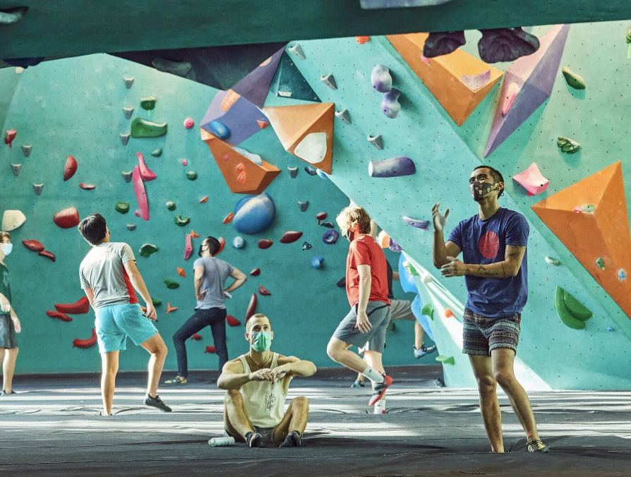 Climbers under a teal bouldering wall with orange and purple volumes