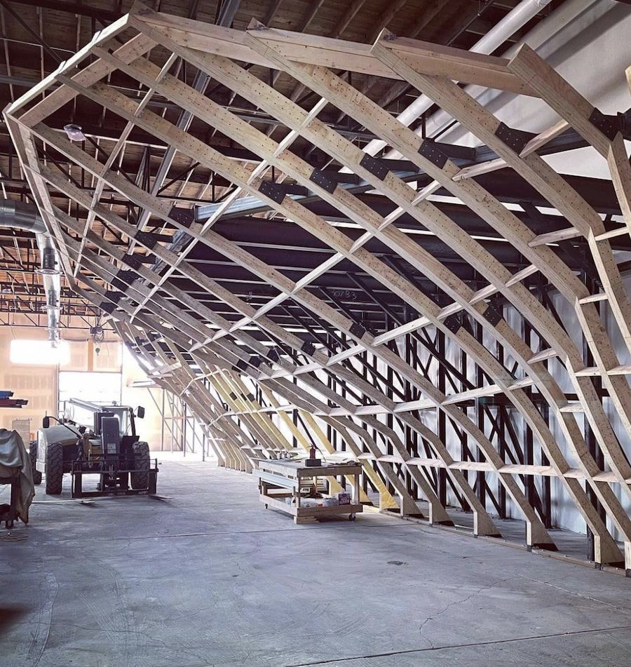 Curved plywood ribs forming the frame of a climbing wall before sheathing, inside a warehouse