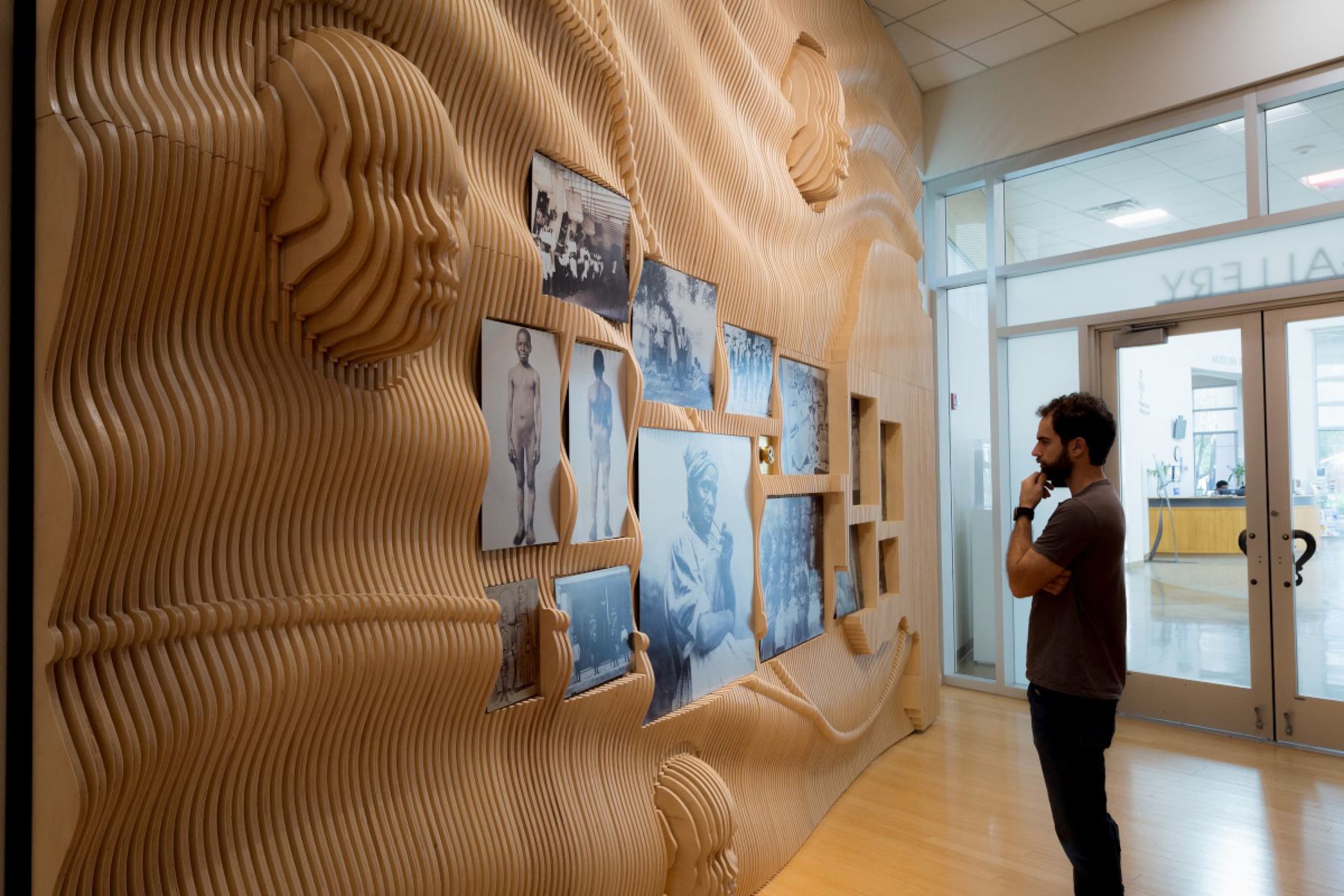 Stacked-slice wood wall with sculpted heads and archival photos