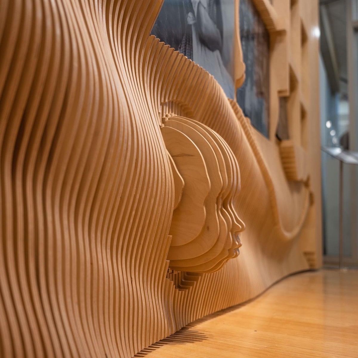 Close view of a head in profile built from stacked wood slices, set into the rippled wall