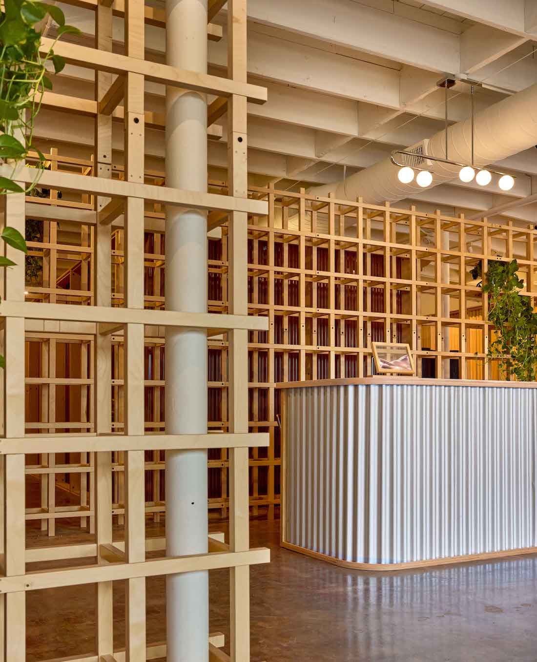 Check-in desk wrapped in silver corrugated metal with a wood top, behind a wood lattice screen and a white column