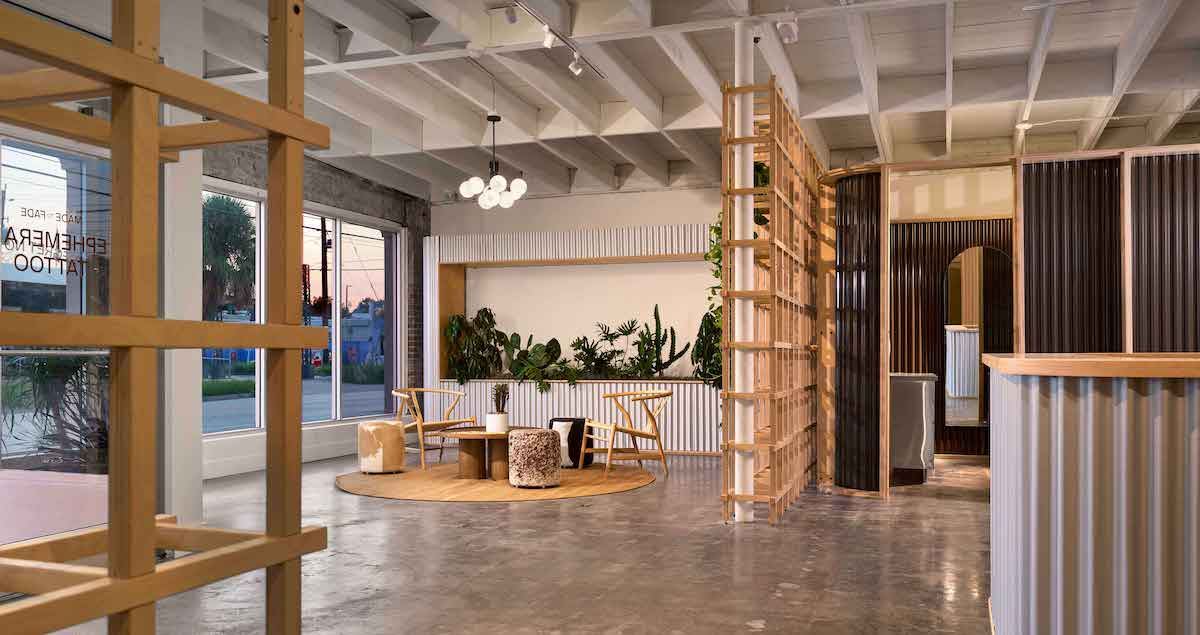 Studio lobby with a wood lattice screen, lounge chairs on a round rug, a planter clad in white corrugated metal, and booths behind