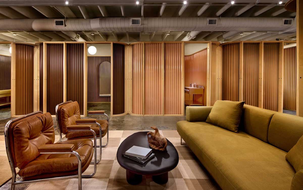 Lounge with leather chairs and a green sofa in front of a row of booths with plywood frames and corrugated panels in tan and brown