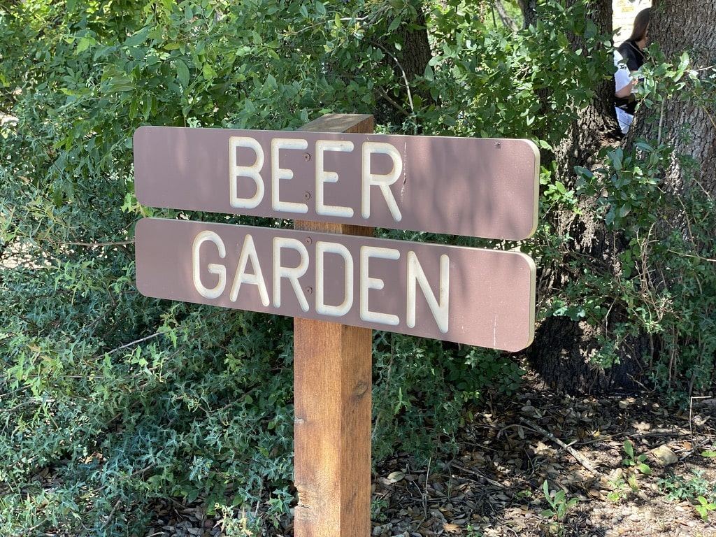 Brown carved sign reading Beer garden on a wood post in front of shrubs