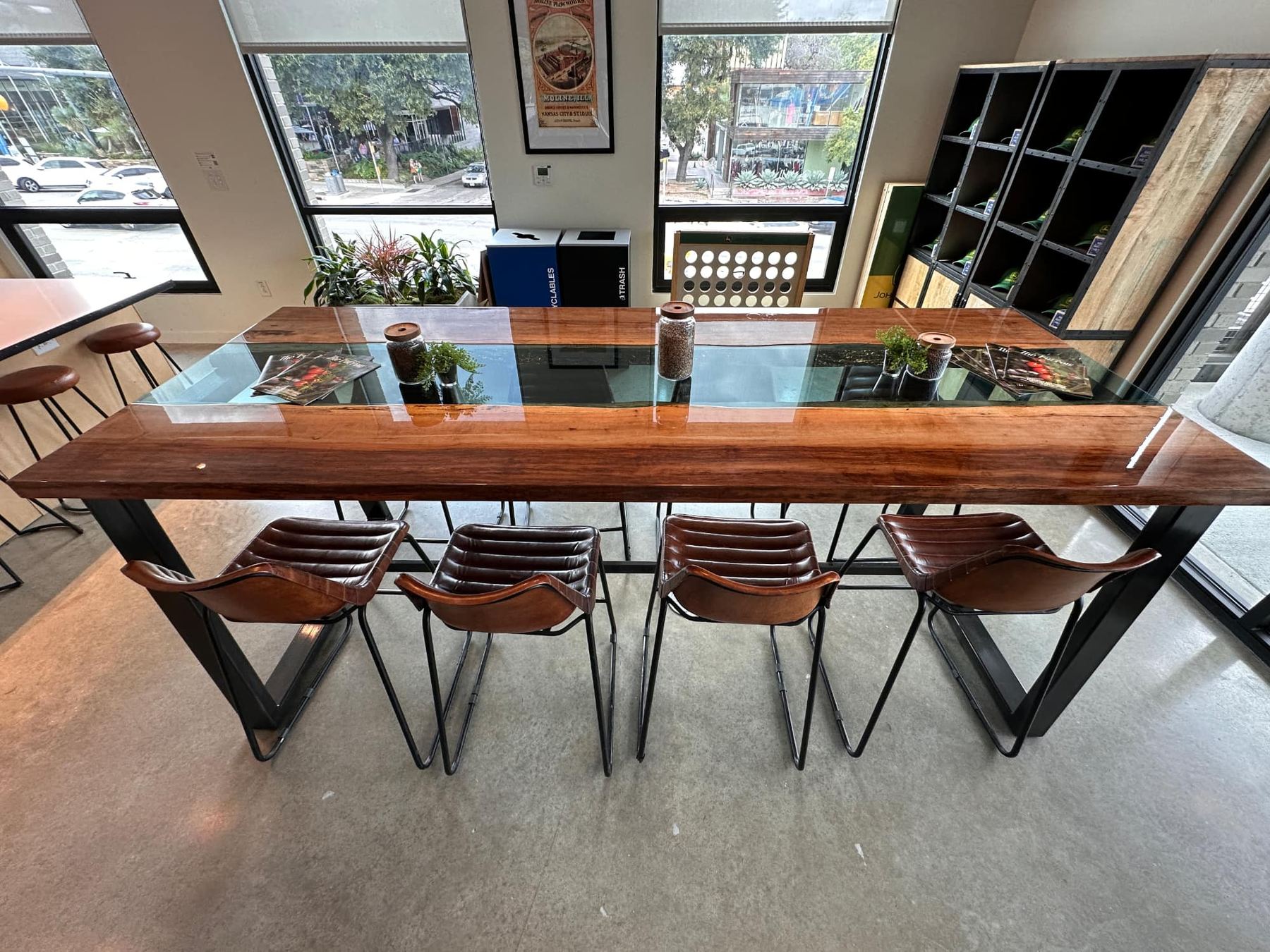 Long live-edge table with a glass center channel, steel legs and leather stools by a window