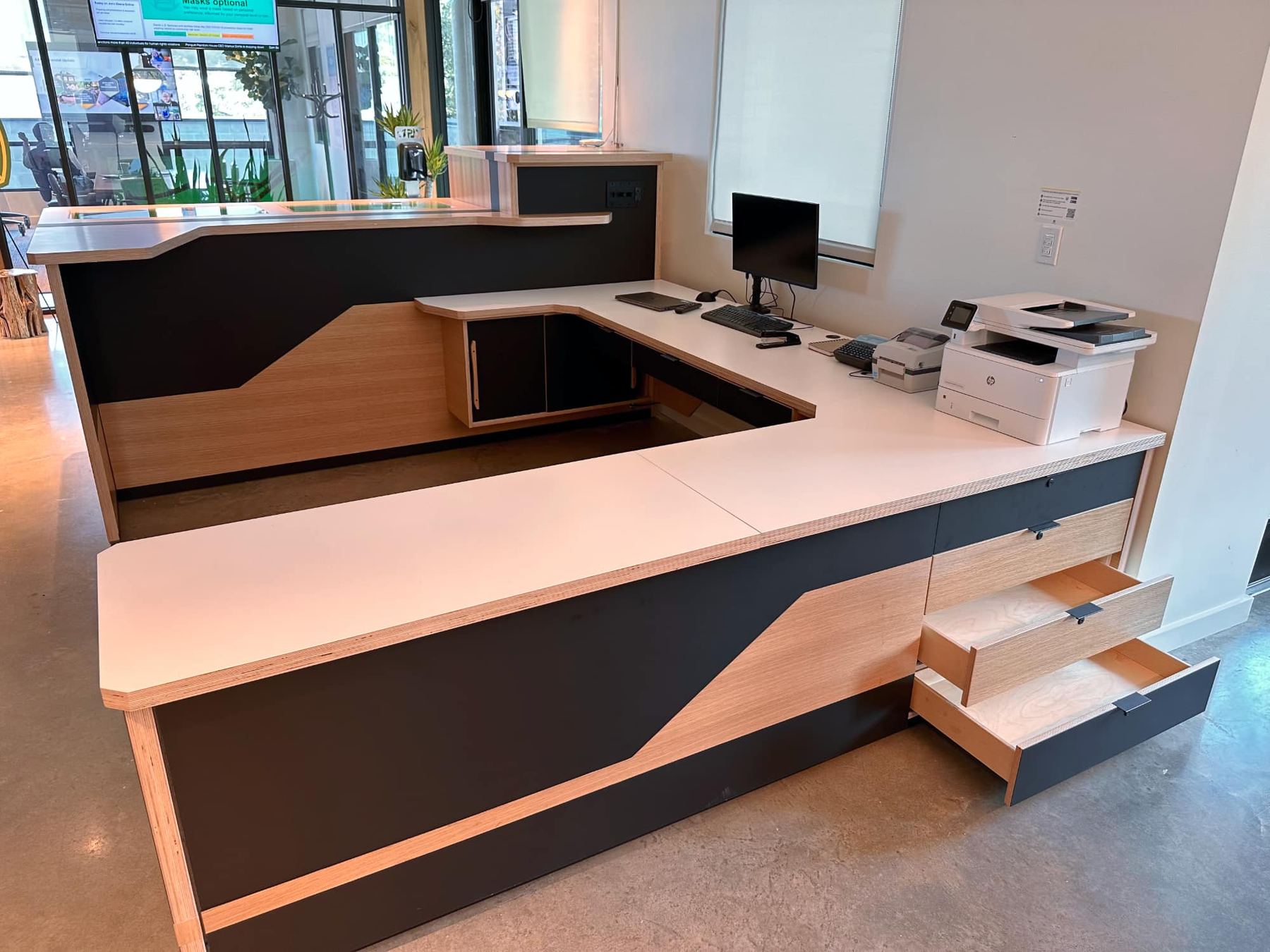 L-shaped counter with a white top, wood and dark gray panels, and drawers, with a printer and monitor on top