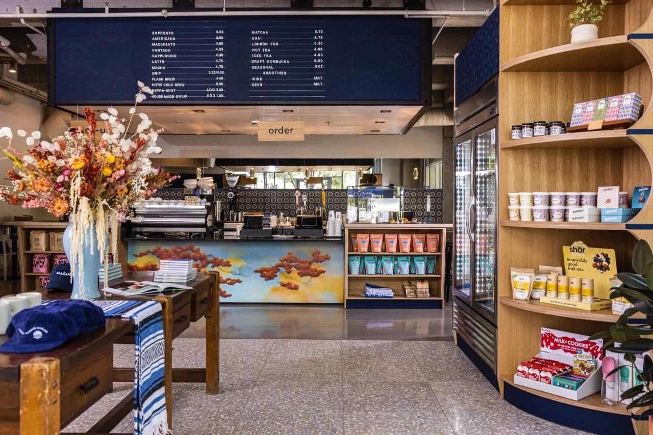 Order counter under a navy menu board, with a mural on the counter front and curved wood shelving to the right
