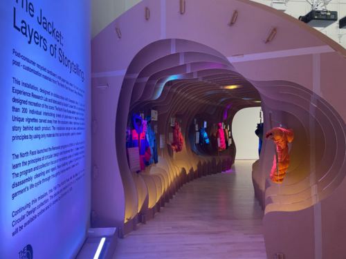 Inside the cardboard tunnel, lit purple and orange, with jackets hanging in niches along the curved walls