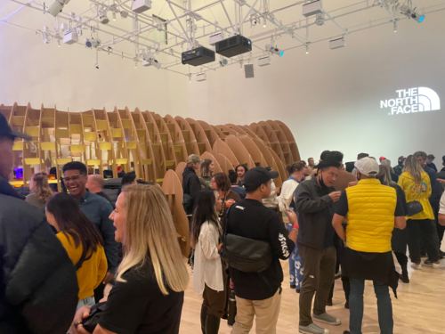 Crowd at the opening beside the cardboard tunnel, with The North Face logo projected on the gallery wall